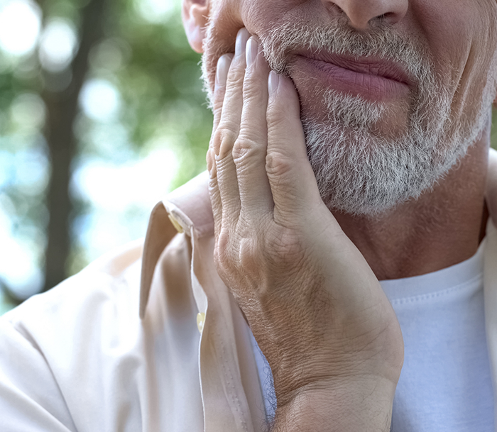 Senior man holding his face in pain before an apicoectomy in Bloomfield