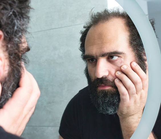 man looking closely at his face in the mirror