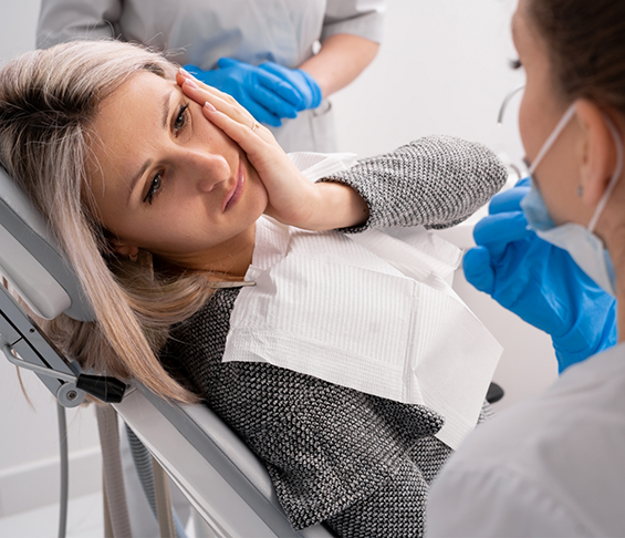 Woman holding her cheek in pain while visiting her emergency dentist