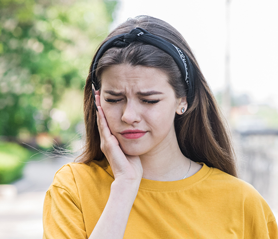 Young woman holding the side of her face and wincing in pain
