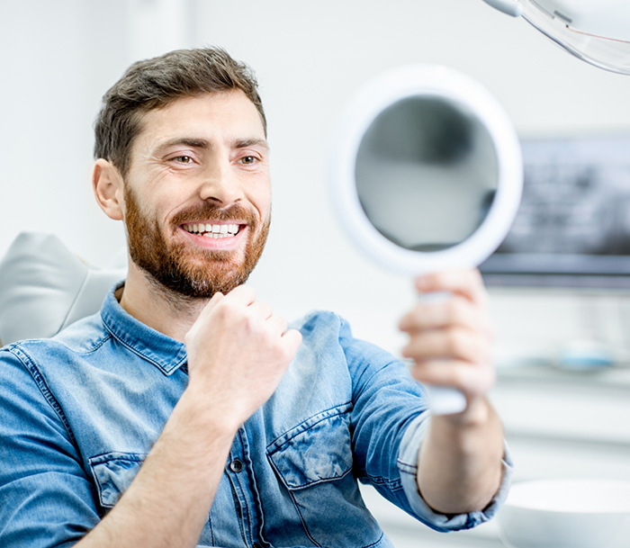 Dental patient looking at his smile in a mirror after endodontic retreatment in Bloomfield