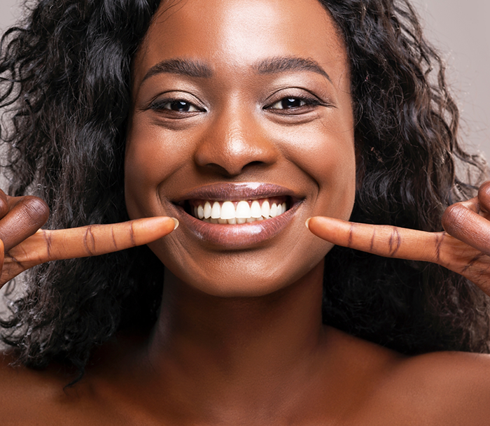 Woman pointing to her bright smile after lightening darkened teeth in Bloomfield