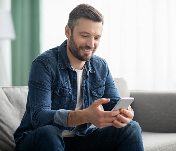 Man sitting on a couch and smiling while looking at his phone